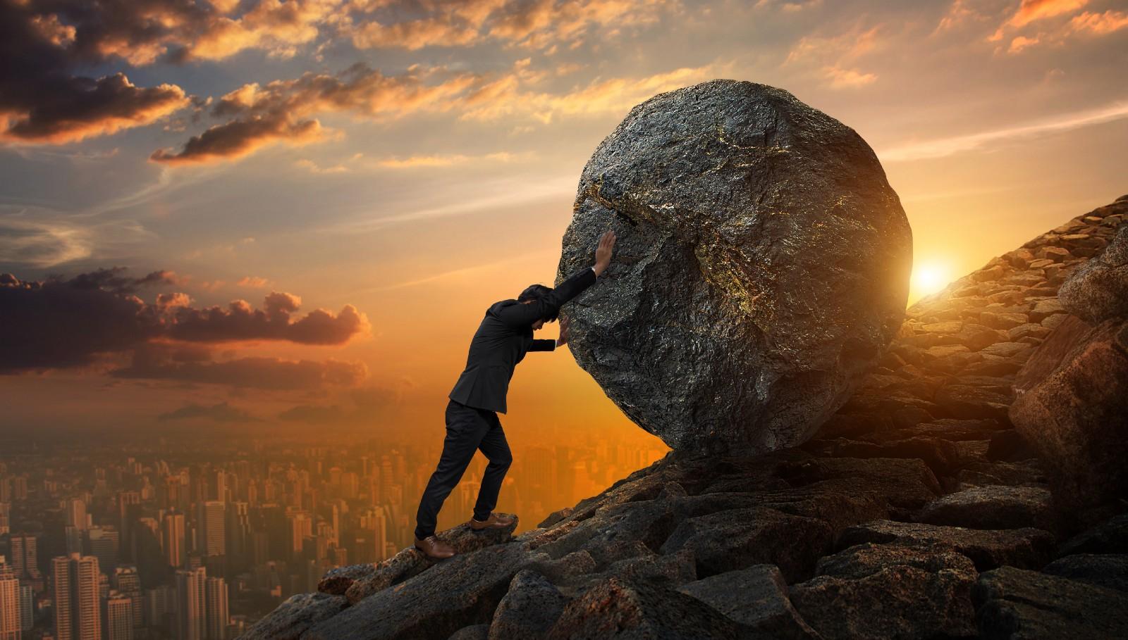 A business man pushing a boulder up a mountain.